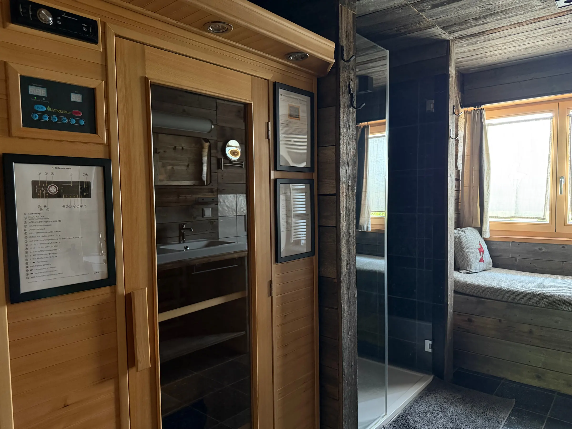 Geöffnete Infrarotkabine mit Holzbank, daneben Dusche und gepolsterte Fensterbank