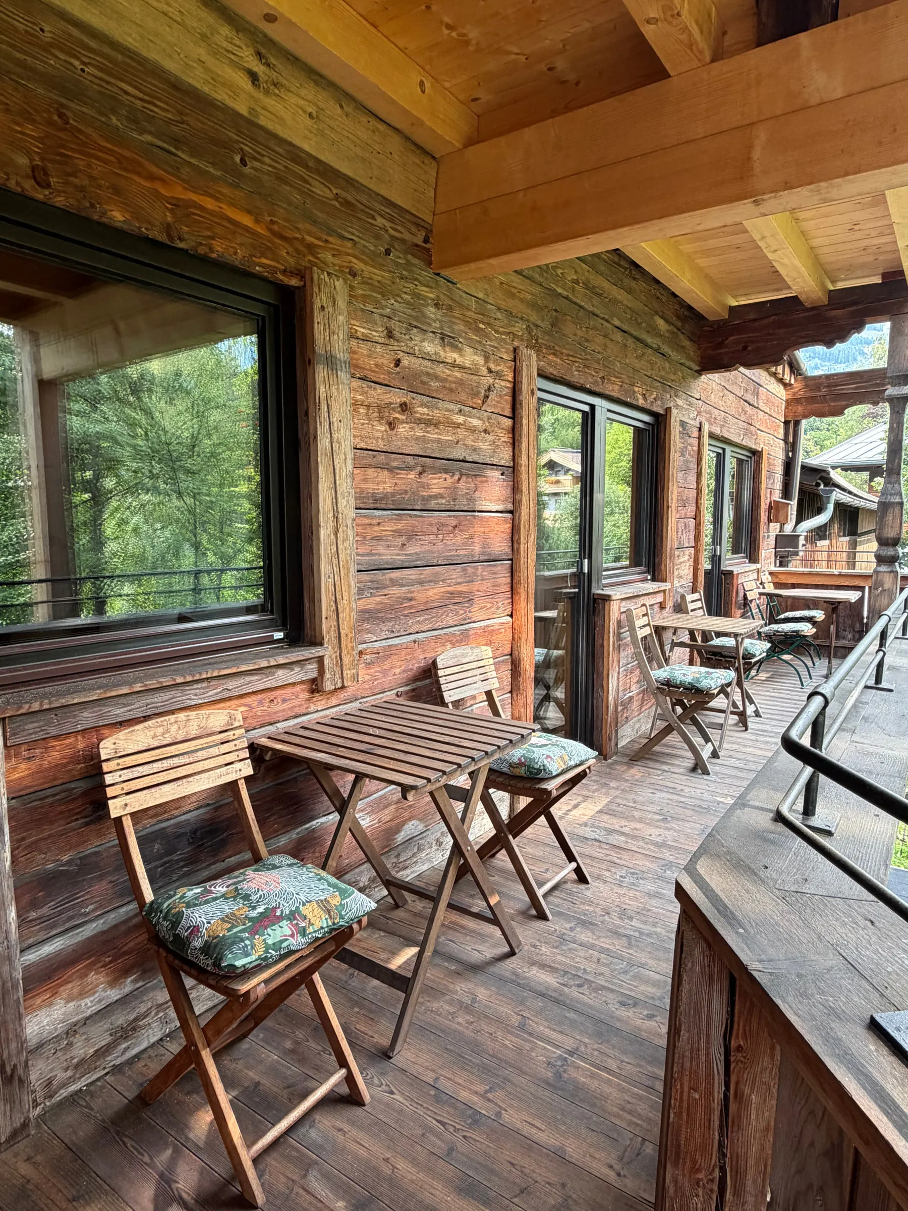 Langer überdachter Balkon aus Holz mit mehreren kleinen Tischen und Stühlen
