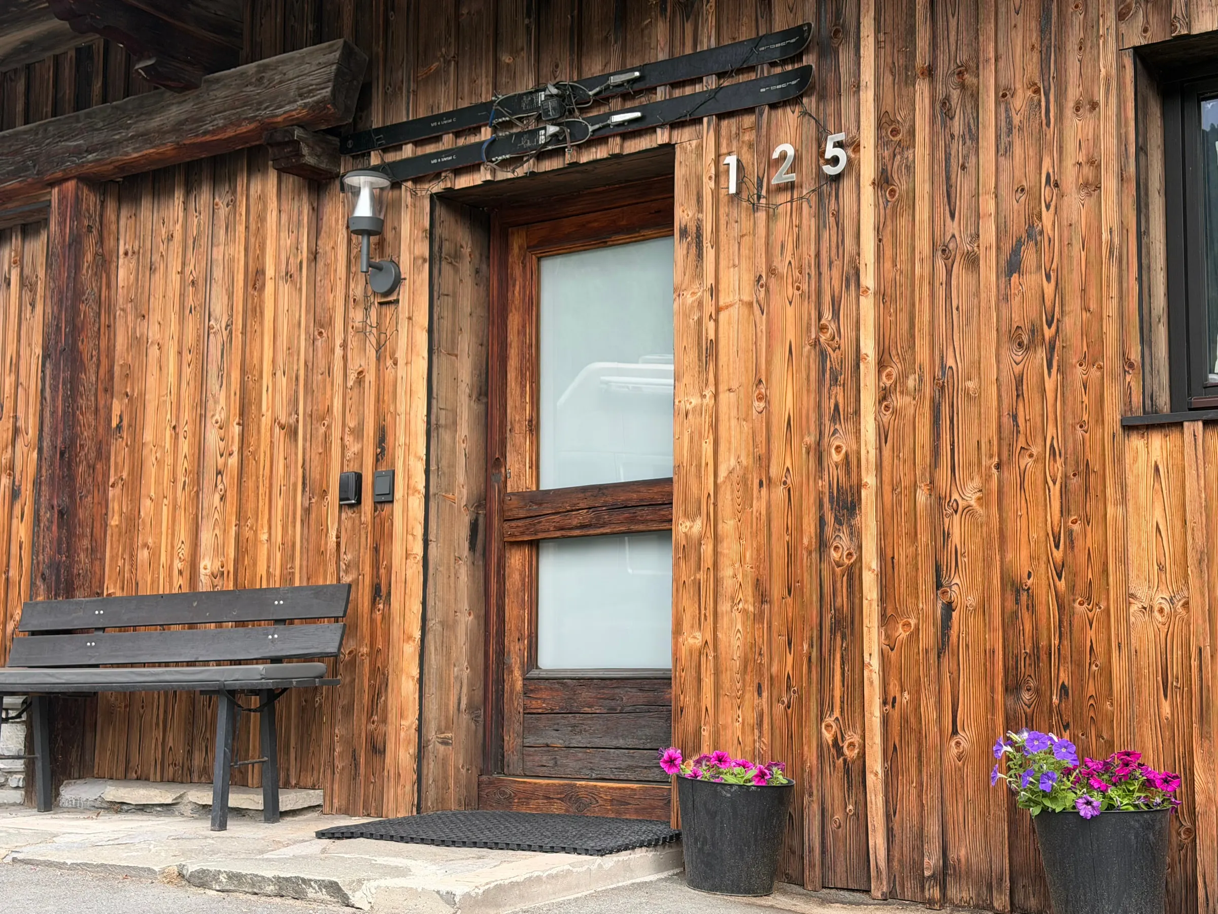 Hauseingang mit verwitterter Holzfassade, alten Holzski über der Tür, einer Bank und Blumenkübeln