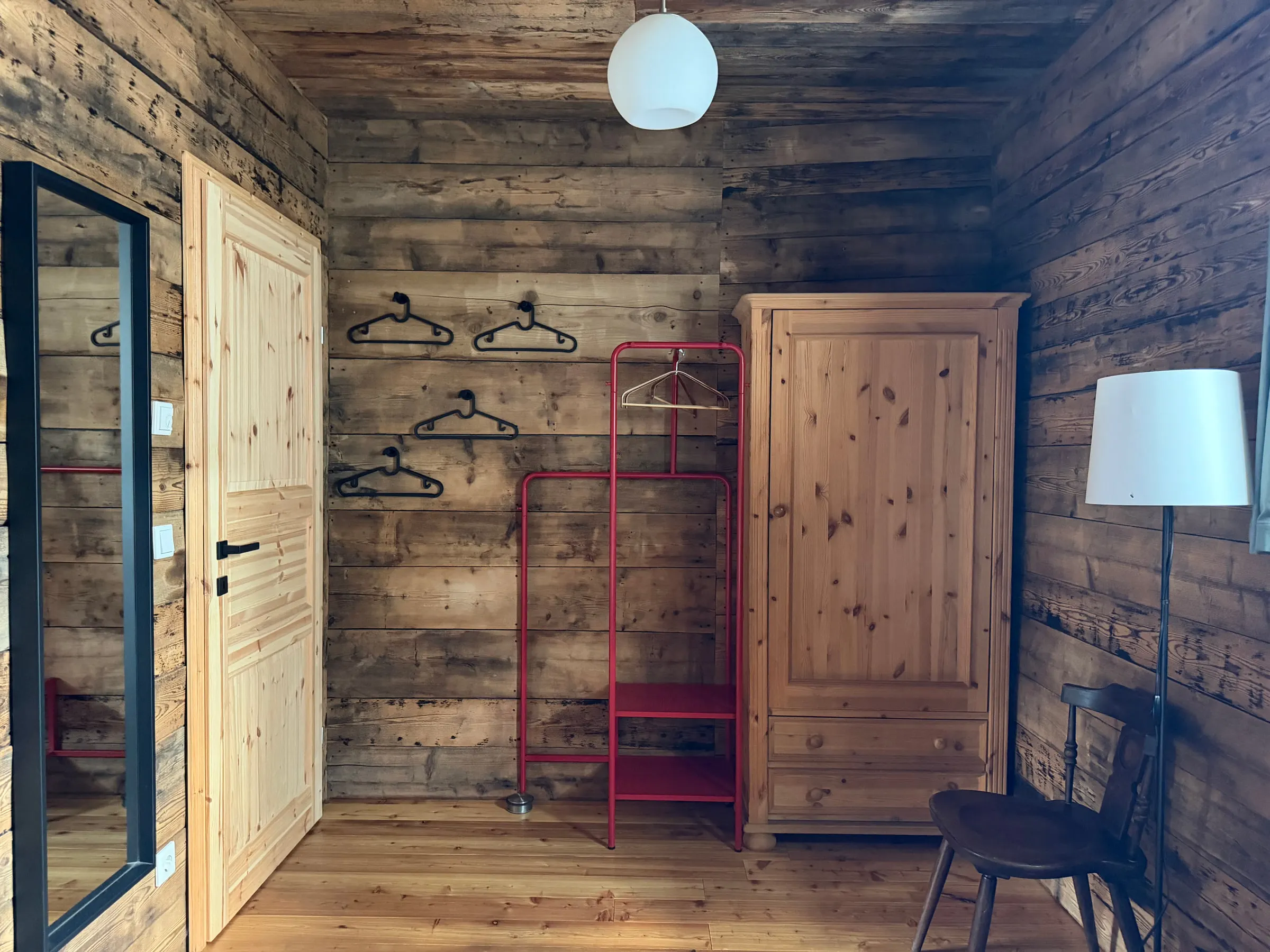 Ecke desselben Zimmers mit Kleiderschrank aus Kiefer, rotem Kleiderständer und Wandhaken