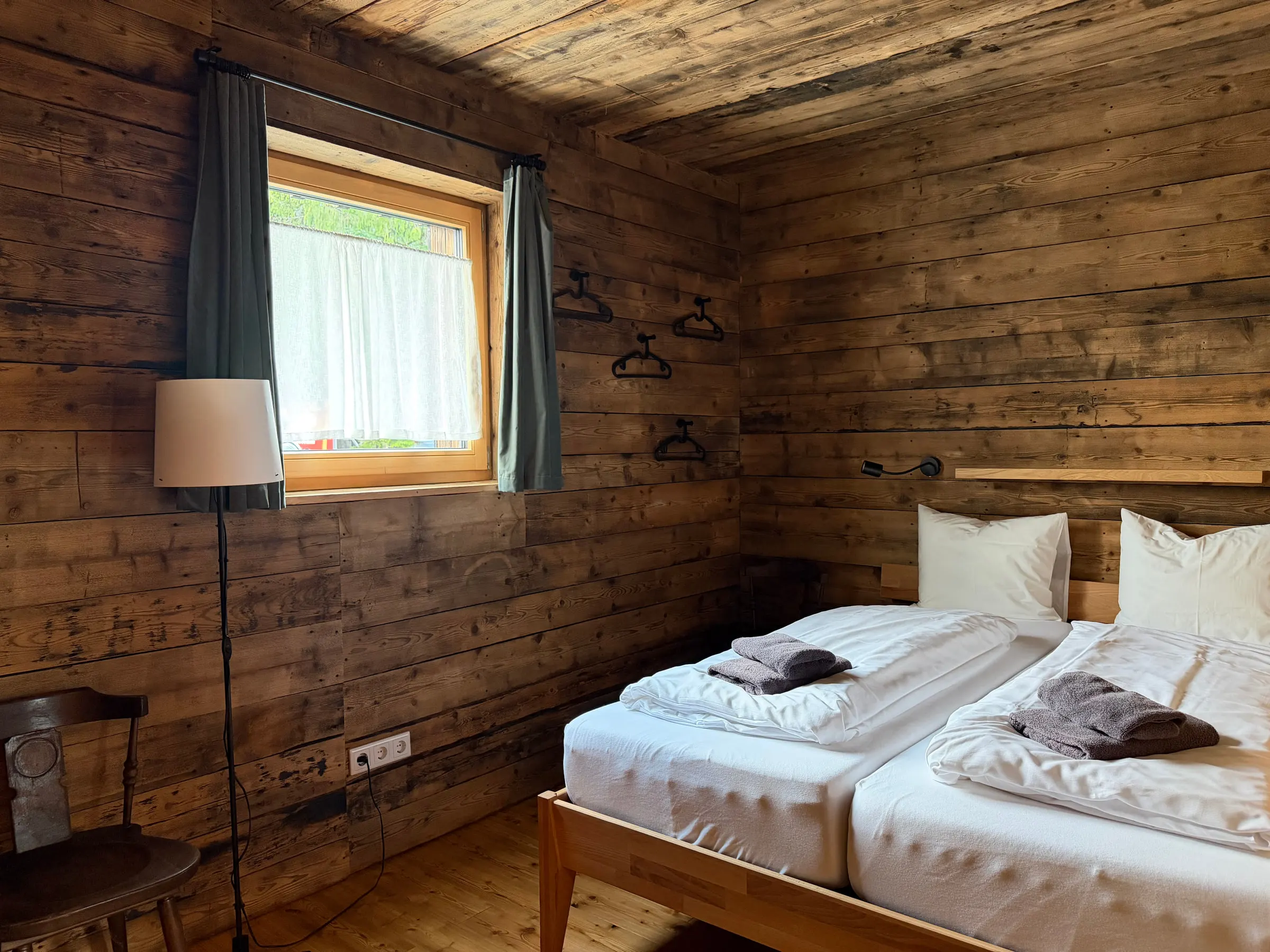 Schlafzimmer mit dunkler Altholzverkleidung, Doppelbett und Fenster mit grünem Vorhang