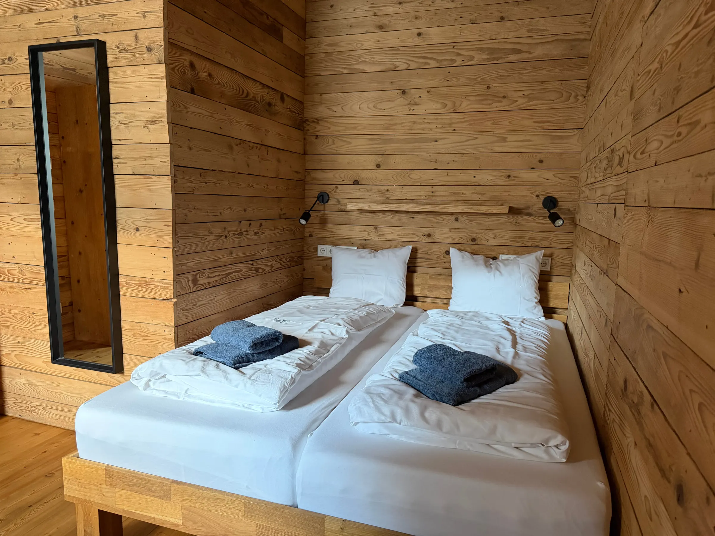 Schlafzimmer mit zwei zusammengeschobenen Einzelbetten, Wandregal mit Leseleuchten und schmalem Spiegel
