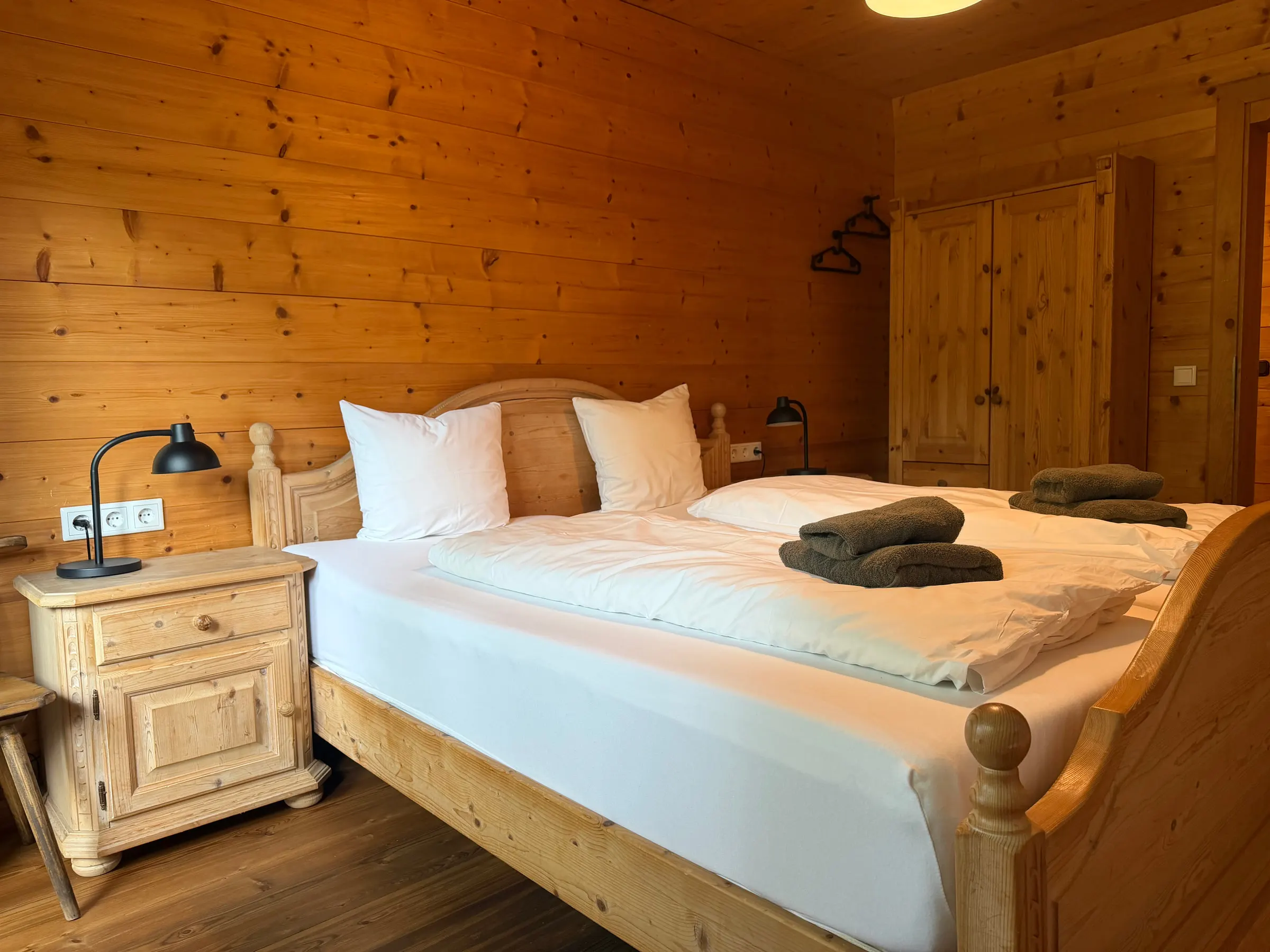 Helles Schlafzimmer mit Bauernbett aus Naturholz, Nachtkästchen und Kleiderschrank