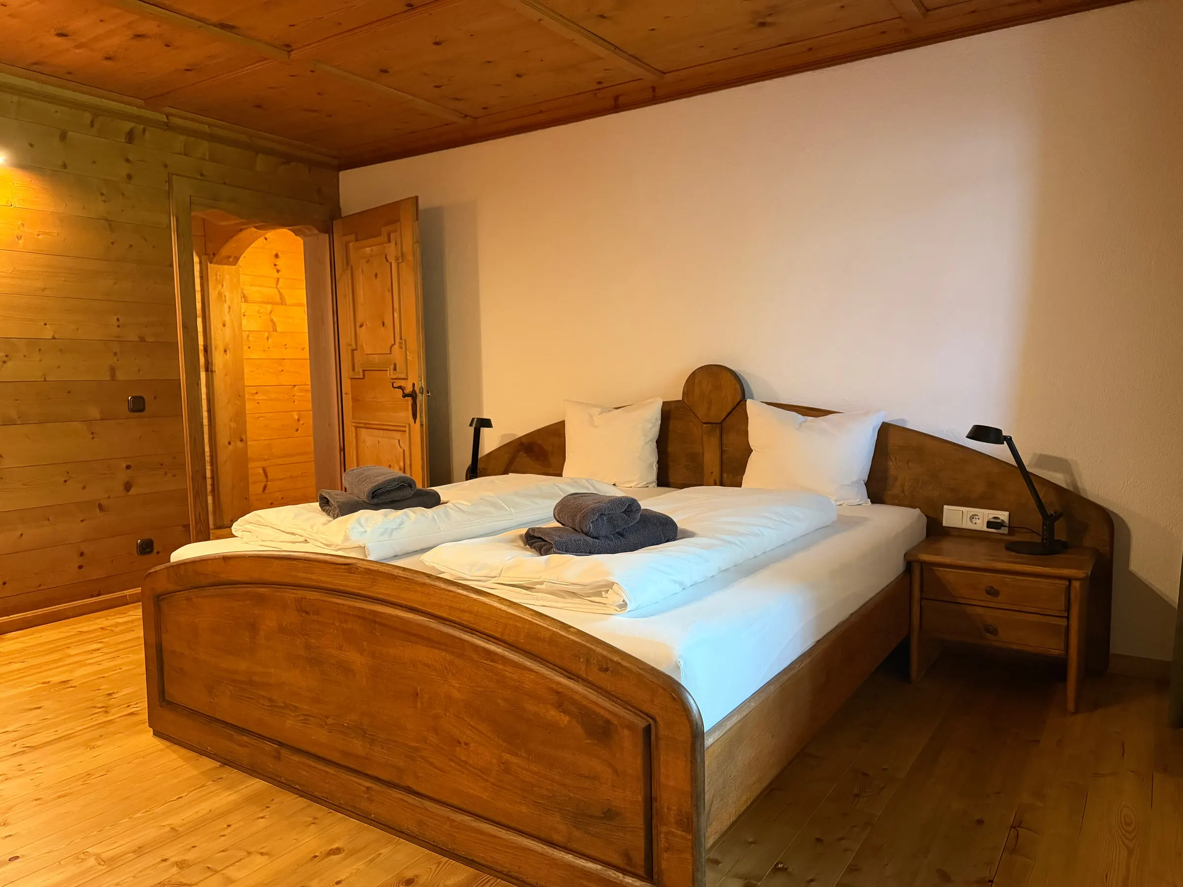 Schlafzimmer mit dunklem Holzbett vor weißer Wand und breiten Dielen