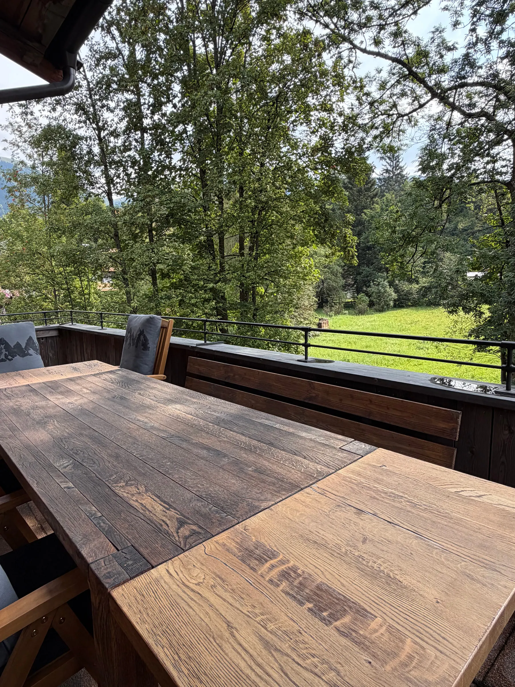 Terrassentisch aus Altholz mit Blick über das Geländer auf eine Wiese und alte Bäume