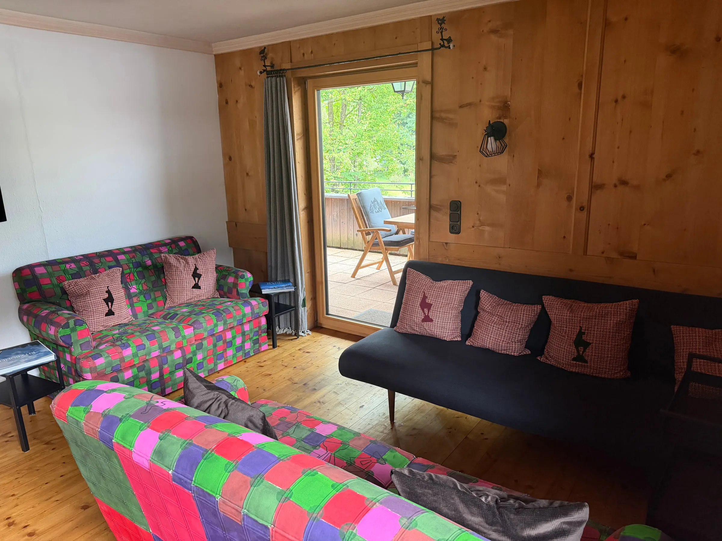 Sitzecke mit zwei bunten Sofas, karierten Kissen und Schiebetür zur Terrasse